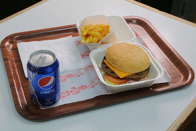 Tray with a burger, fries and a fizzy drink on a table